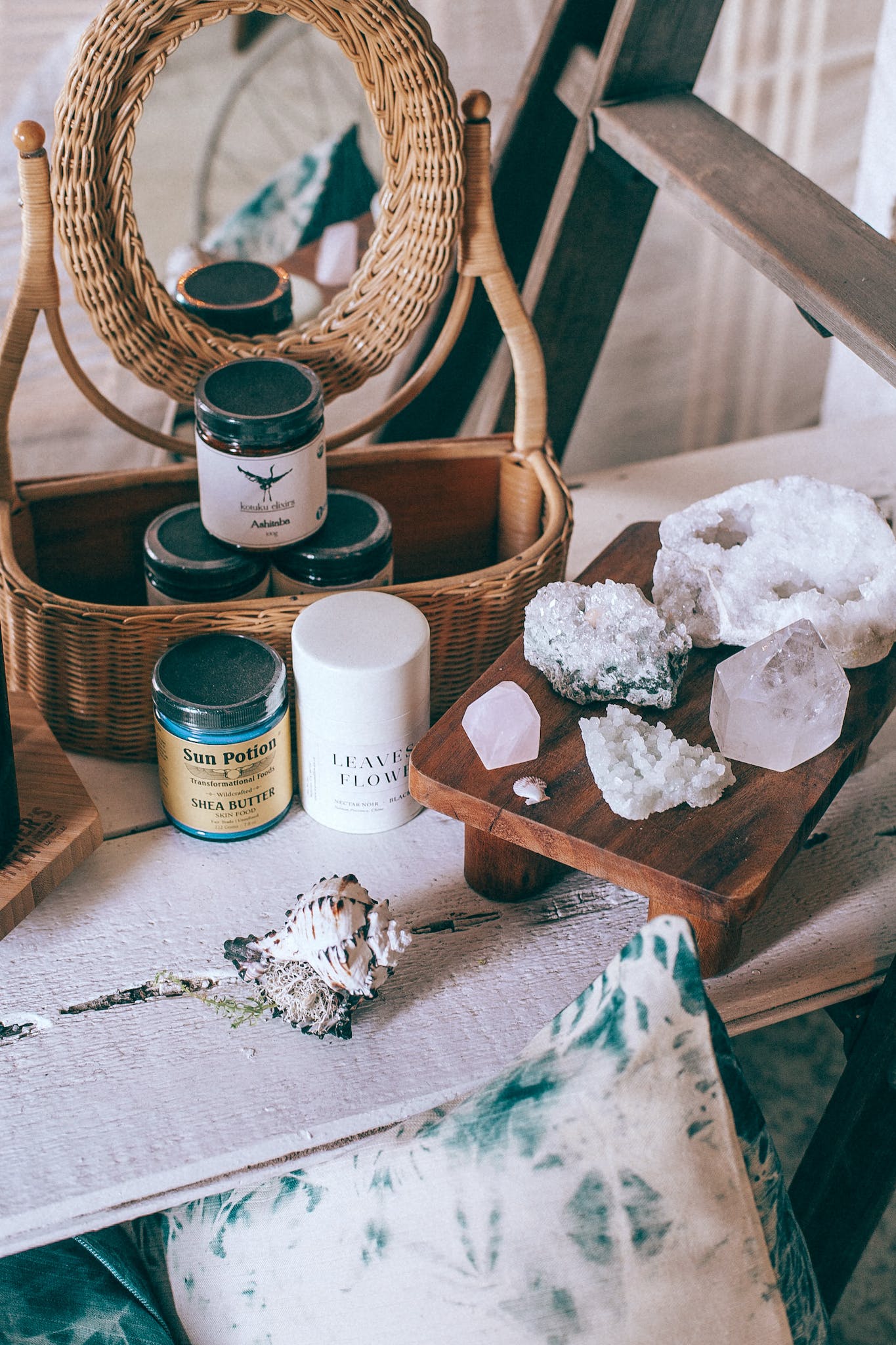 From above of beauty jars in wicker basket reflecting in mirror near sea shell and collection of crystals